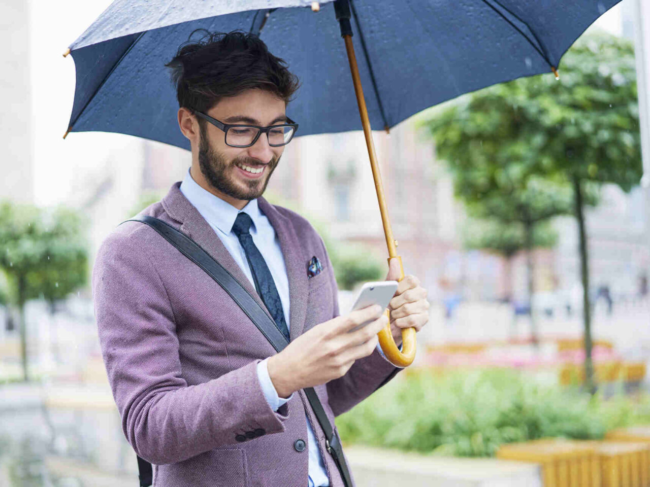 Fashionable businessman with umbrella checking his cell phone in the city